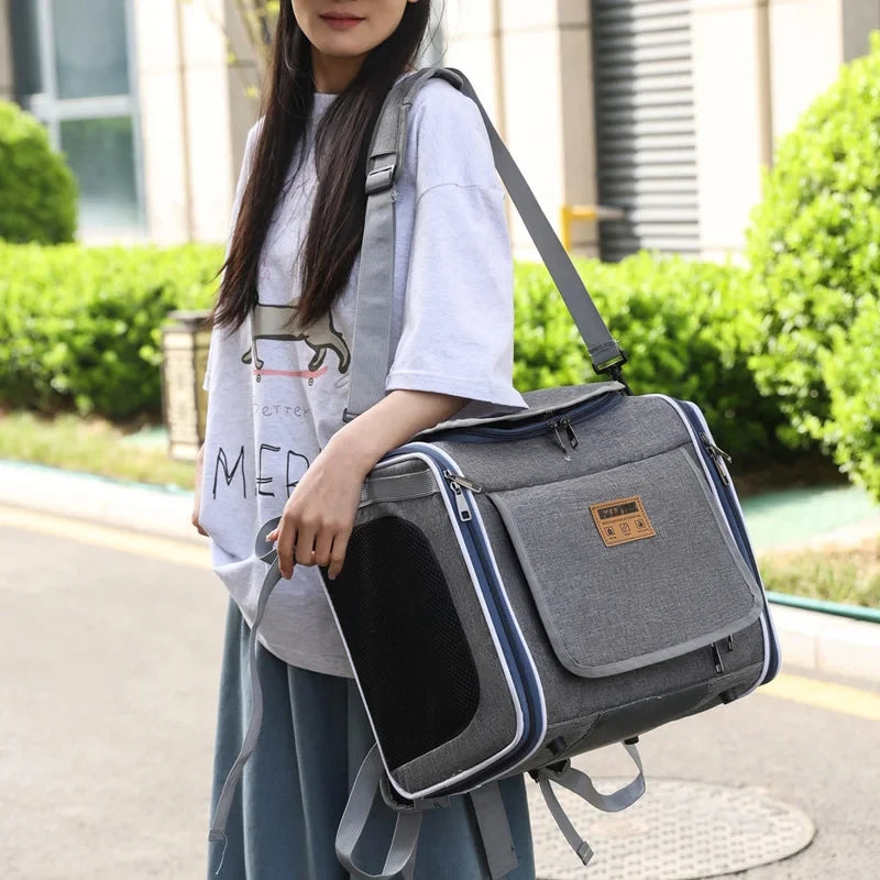 Person holding a gray pet carrier with a visible brand logo outdoors.