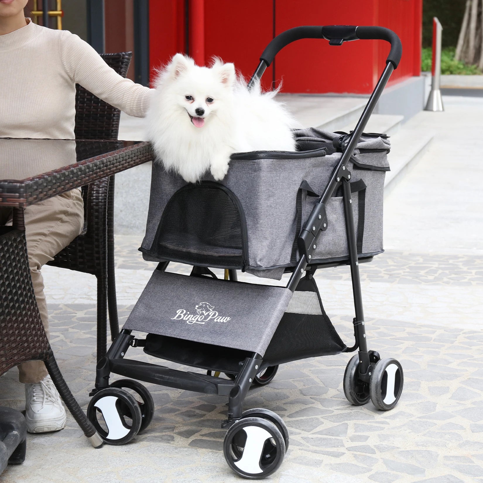 White dog in a gray pet stroller with 'Bing Paw' branding on a sidewalk.