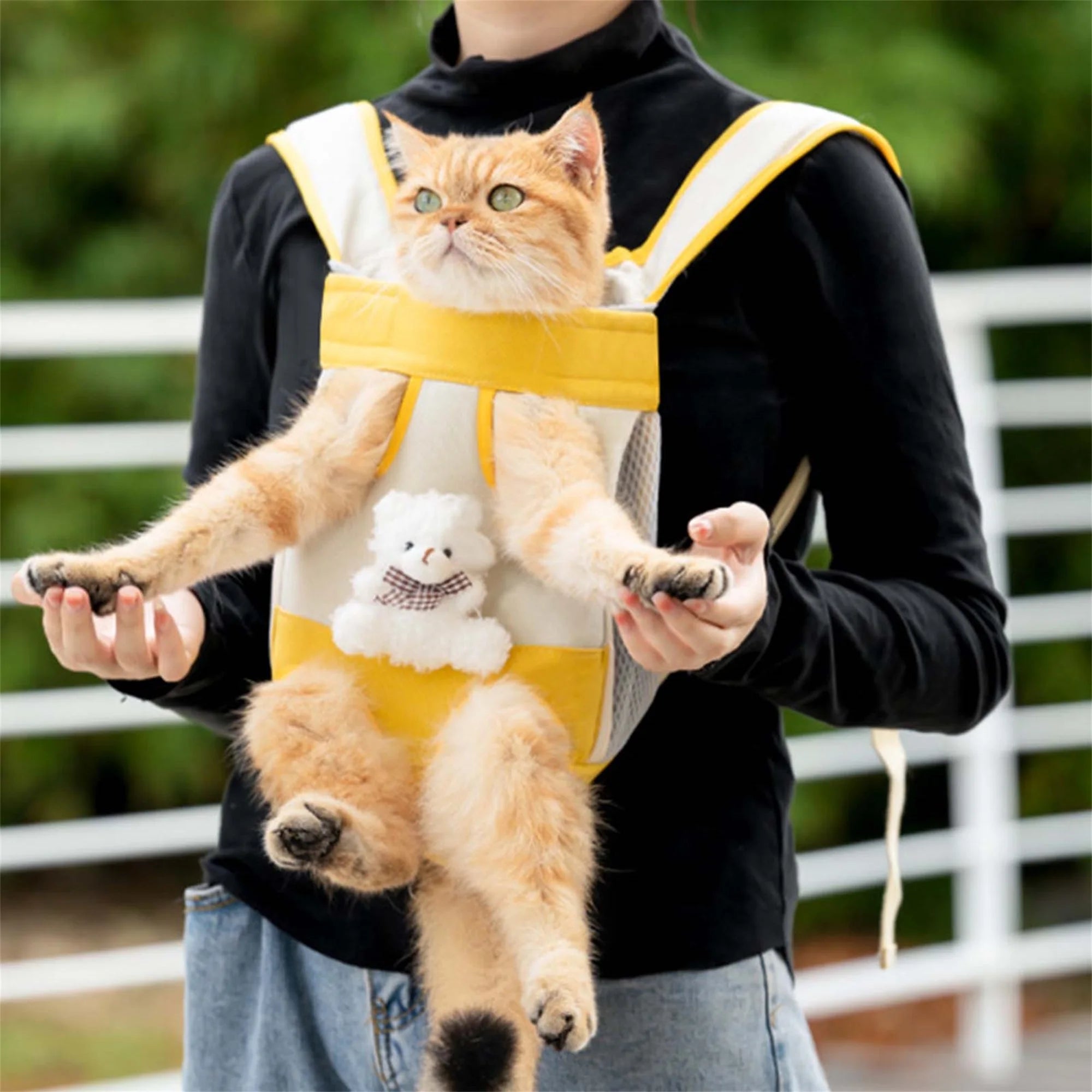 Person holding a cat in a yellow carrier with a teddy bear design outdoors.