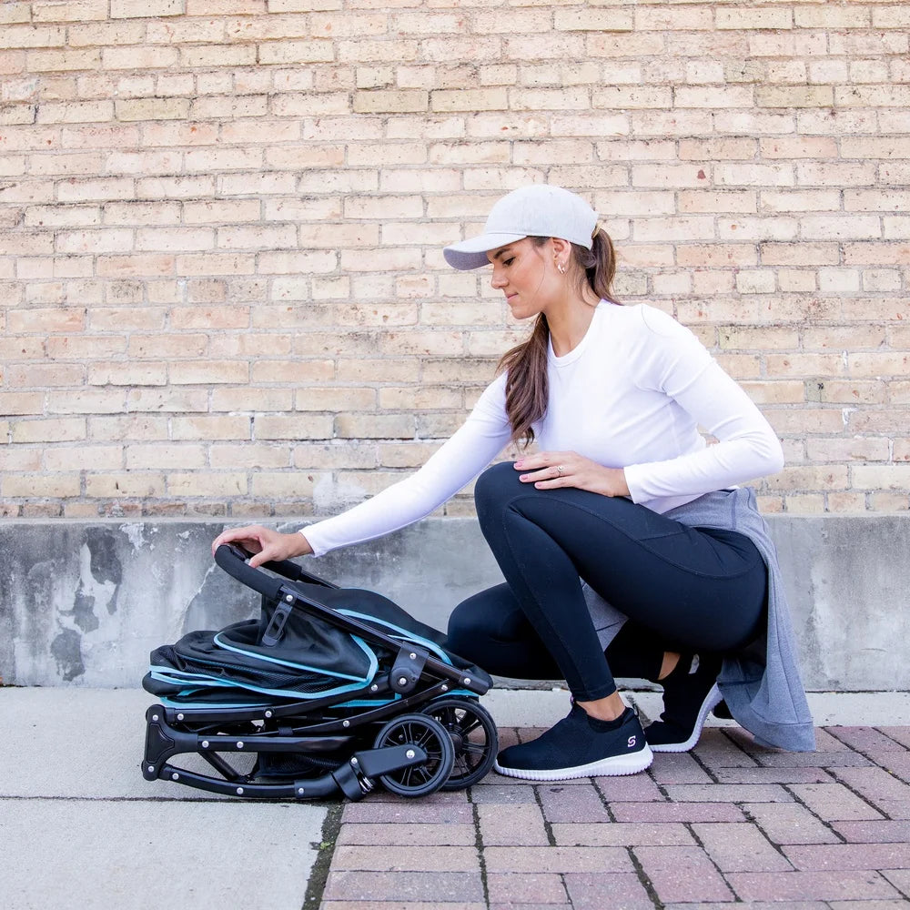Woman adjusting a black baby stroller against a brick wall.