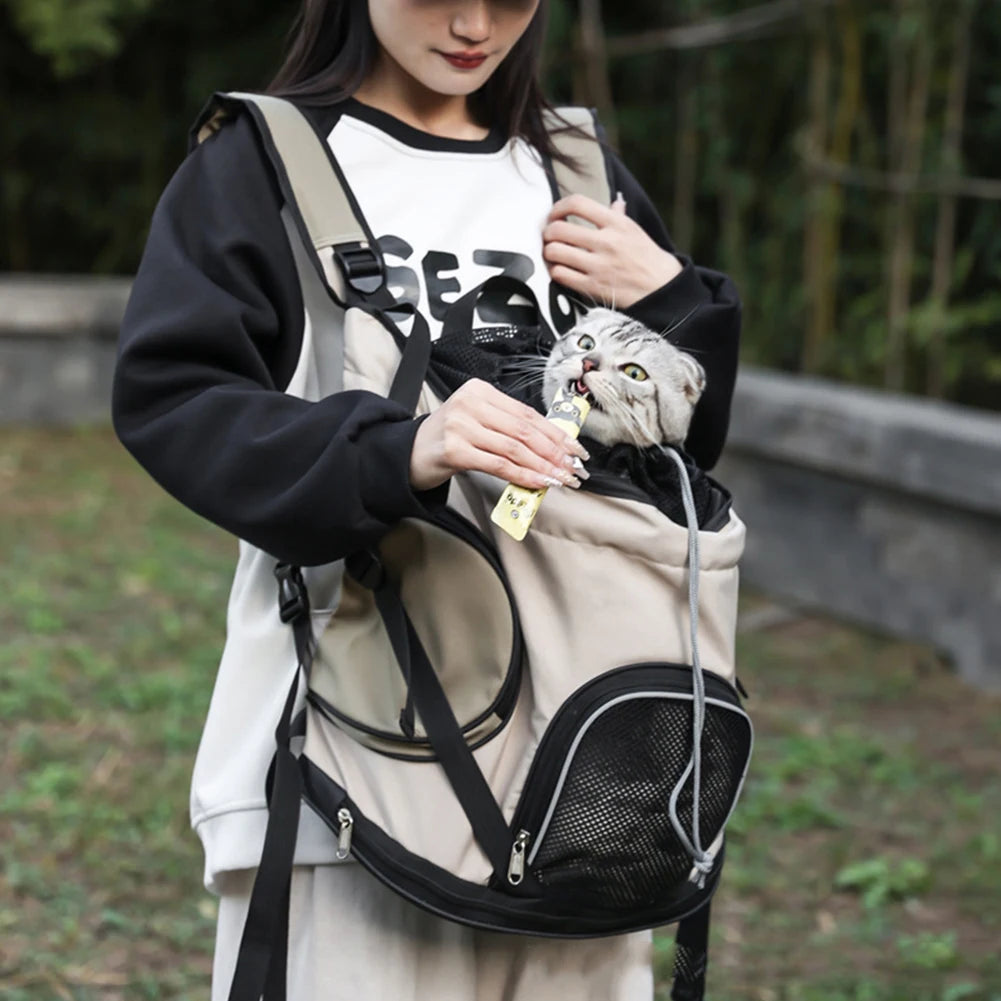 Person holding a small cat in a pet carrier backpack outdoors.