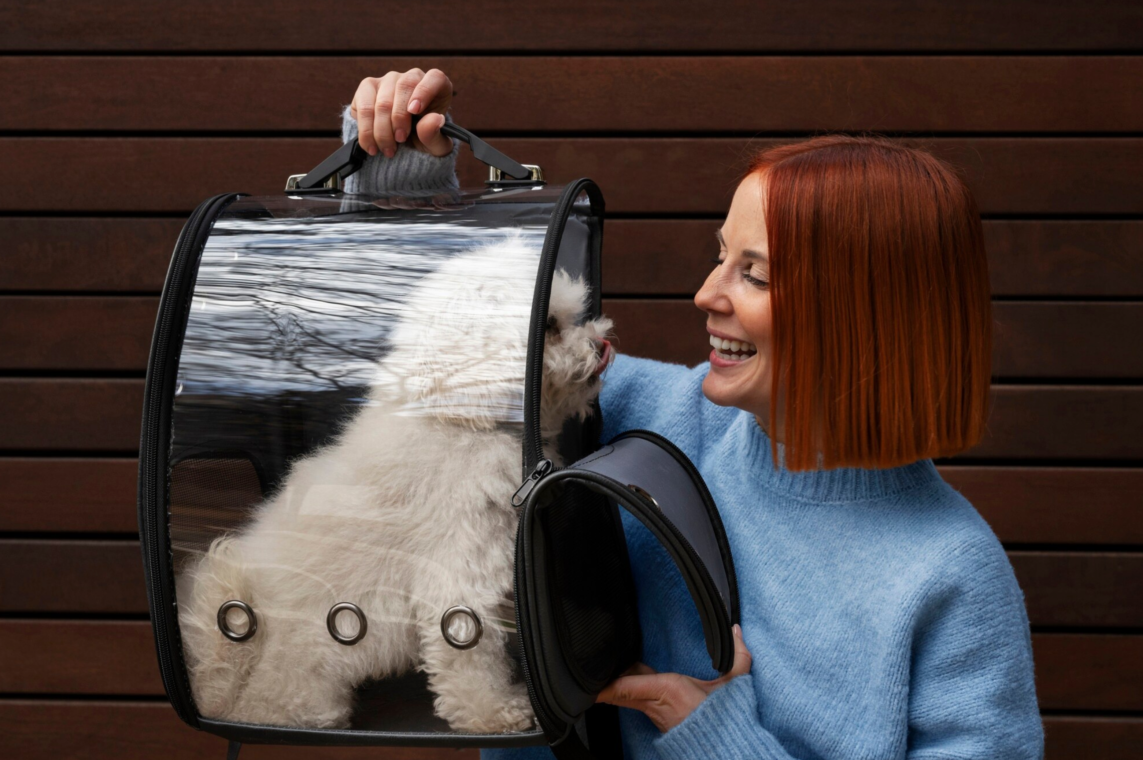 Woman holding a pet carrier with a dog peeking out against a wooden background