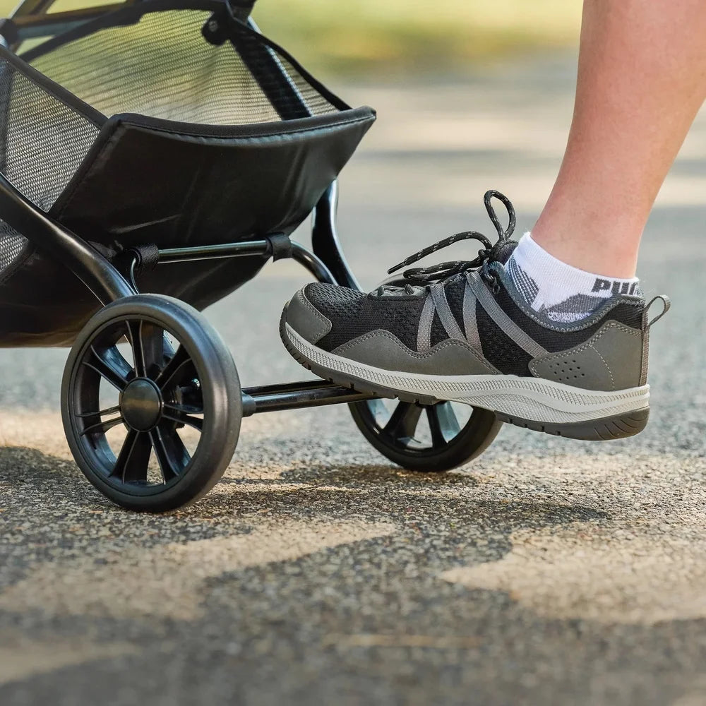 Person wearing gray athletic shoes with a stroller in the background