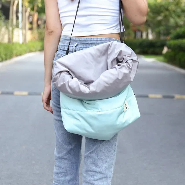 Person holding a light blue and gray bag outdoors on a road.