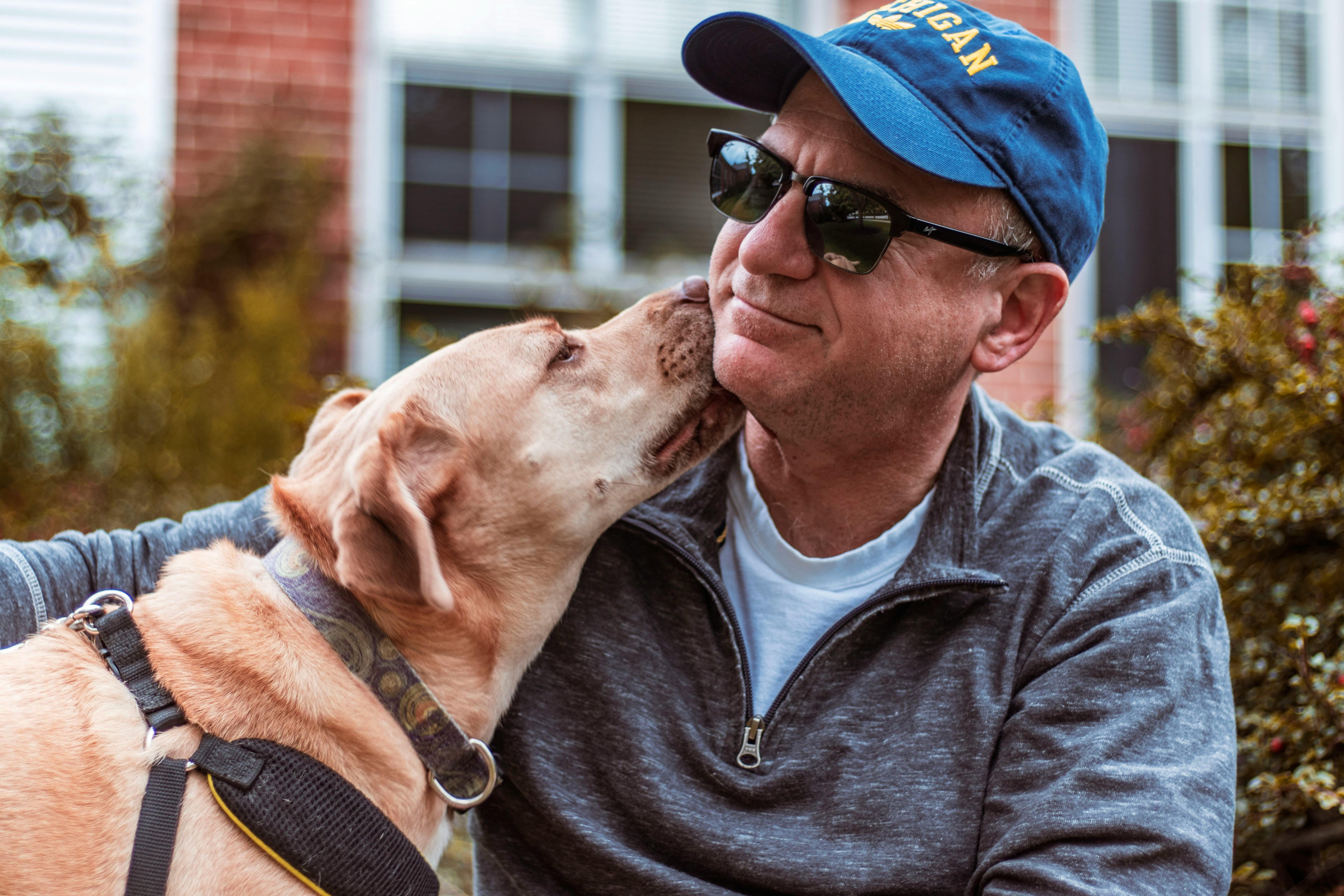 Man wearing a blue cap and sunglasses interacting with a dog outdoors.