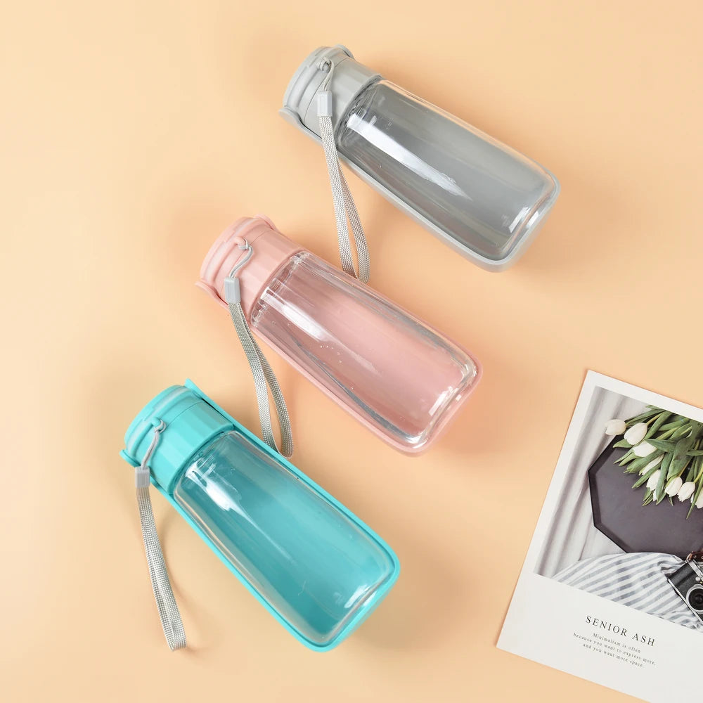 Three transparent water bottles in blue, pink, and gray on a beige background.