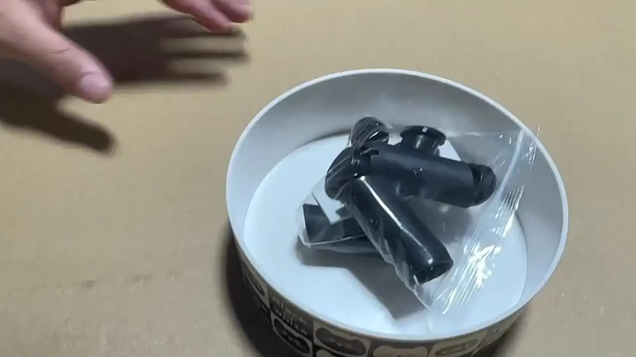 Black hair clips in a clear plastic bag inside a white bowl on a beige surface.