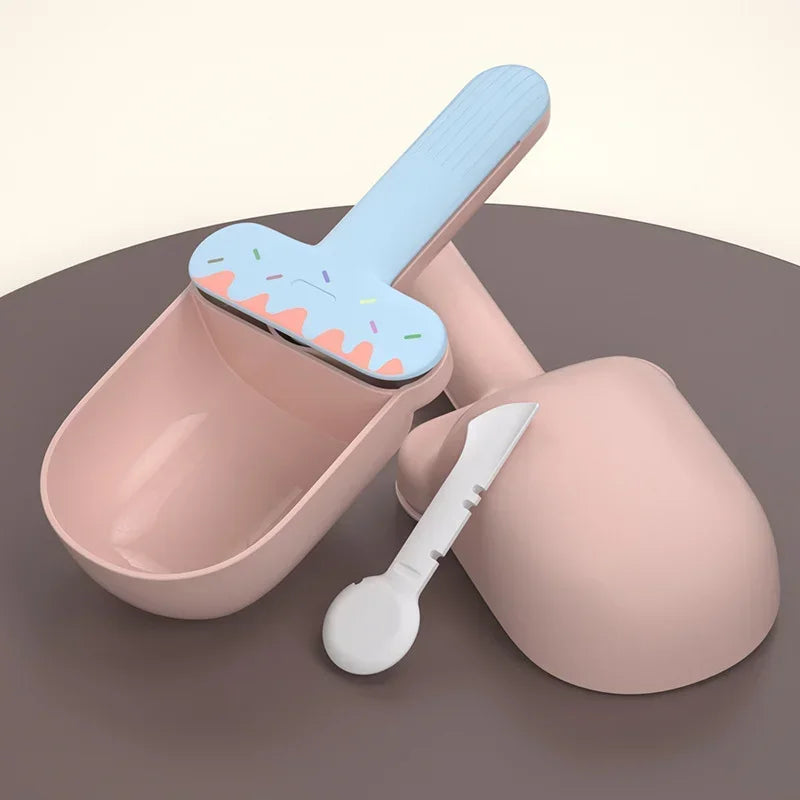 Pink ice cream mold with blue scoop and white spoon on a dark surface