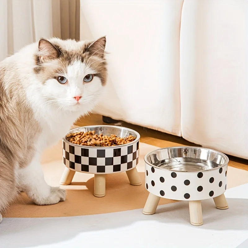 Cat standing next to two pet bowls with checkered and polka dot patterns on a light-colored floor.