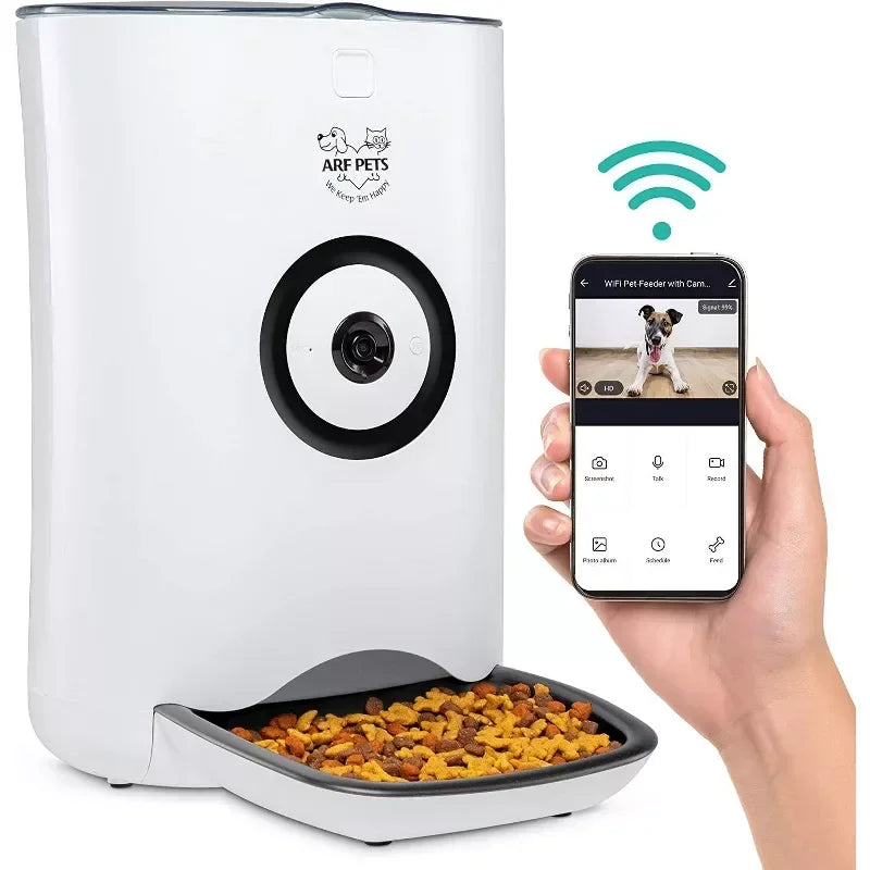 White pet feeder with camera and food tray, accompanied by a smartphone displaying the ARF Pets app.